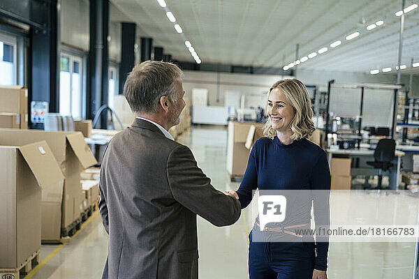 Happy businesswoman handshaking with colleague at warehouse