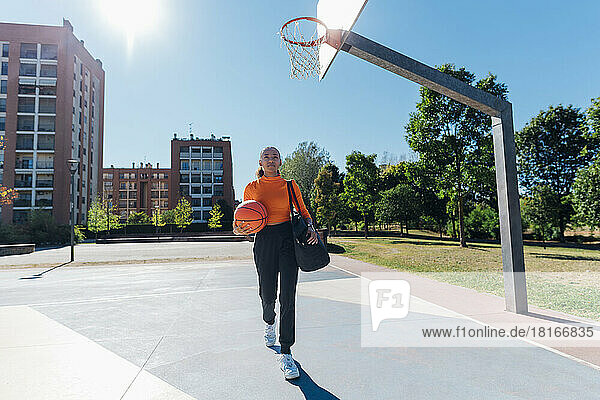 Young sportswoman with basketball walking in sports court