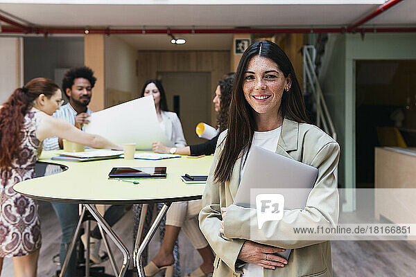 Portrait of a smiling brunette businesswoman holding laptop in office