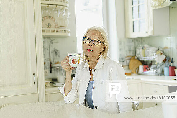 Woman holding cup sitting in kitchen at home
