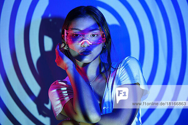 Young woman wearing LED smart glasses standing in front of wall under spiral shadow