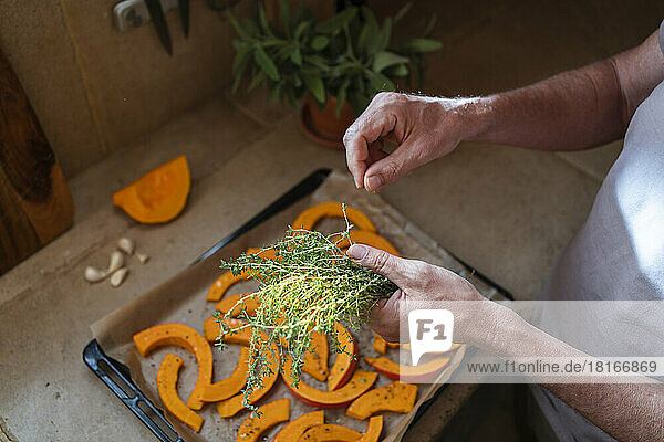 Hands of man picking thyme over slice of pumpkin in tray