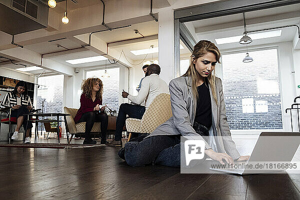 Young businesswoman using laptop sitting on office floor