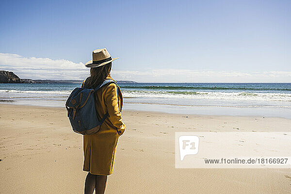 Reife Frau mit Rucksack steht an einem sonnigen Tag am Strand