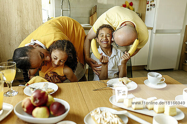 Parents kissing children at dining table in kitchen