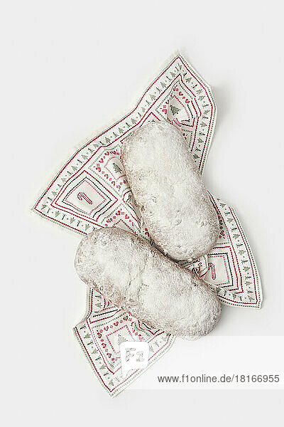 Set of Christmas stollen cakes with icing sugar on table napkin against white background