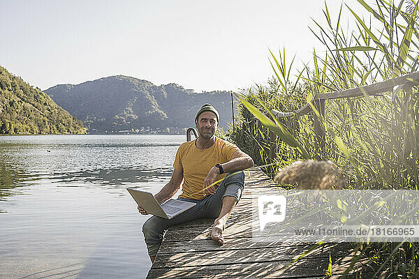 Mature freelancer with laptop on jetty by lake