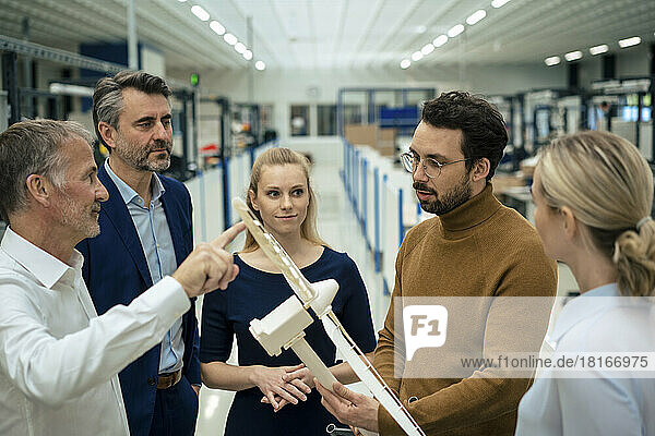 Senior businessman discussing over wind turbine model with colleagues in industry
