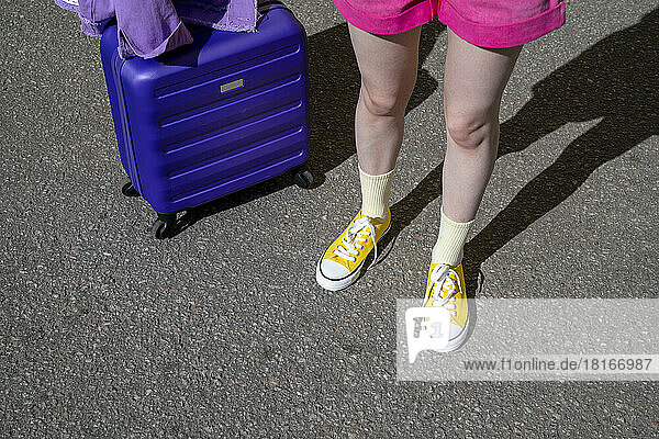 Woman wearing canvas shoes standing with luggage on road