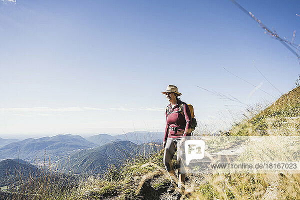 Reife Frau mit Hut spaziert mit Rucksack auf dem Berg
