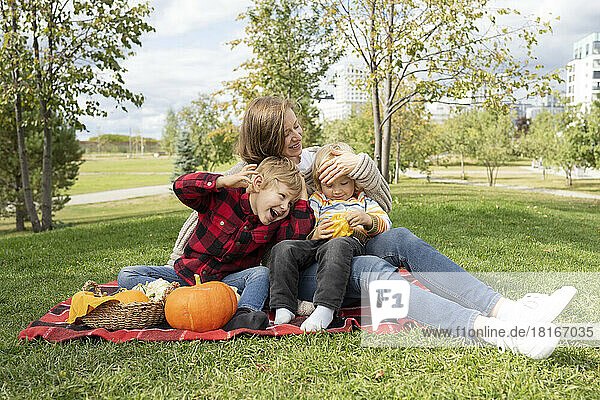 Glückliche Jungen mit Mutter  die auf einer Picknickdecke im Park sitzt