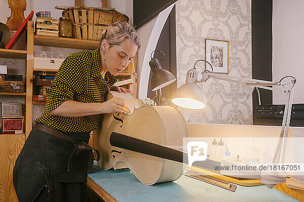 Gitarrenbauer mit Handwerkzeug arbeitet am Kontrabass und steht am Schreibtisch in der Werkstatt