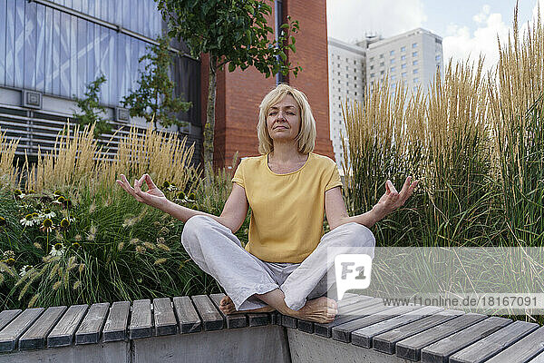 Mature woman with eyes closed meditating on bench