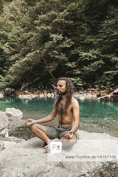 Shirtless young man meditating on rock