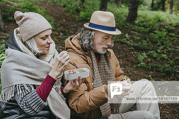 Couple having salad from lunch box in forest