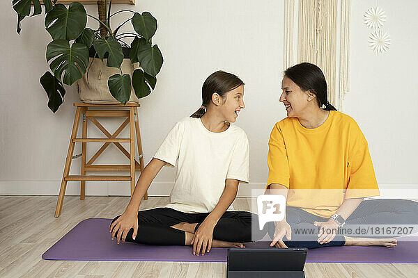 Happy girl looking at mother sitting on exercise mat in front of tablet PC