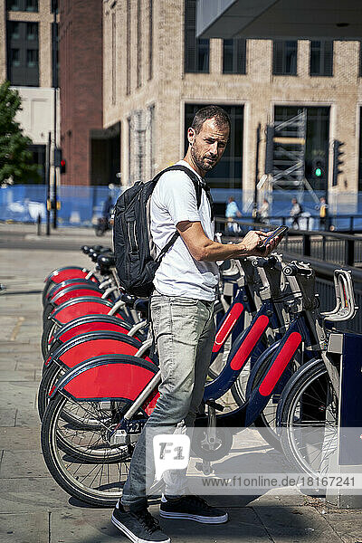 Mann mit Smartphone mietet an sonnigem Tag ein Fahrrad am Parkplatz
