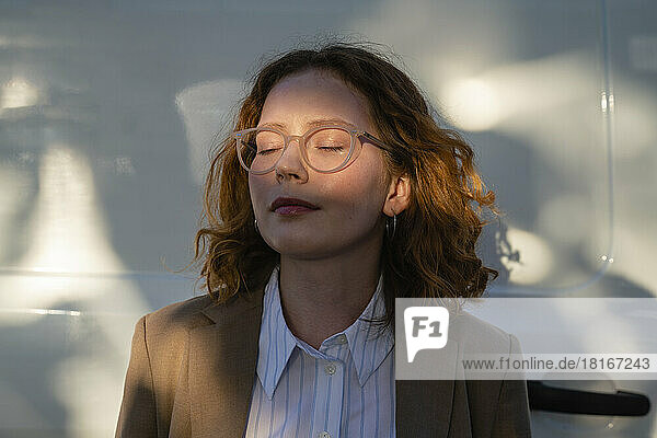 Young businesswoman with eye closed in sunlight