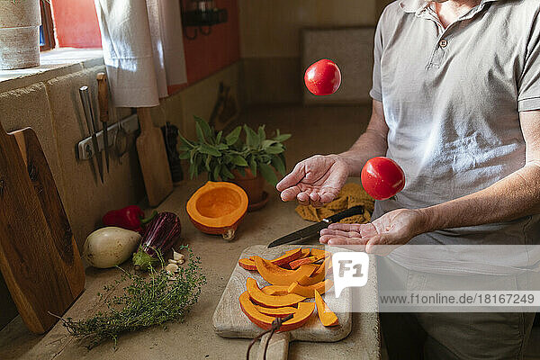 Hands of man juggling with tomatoes at kitchen counter