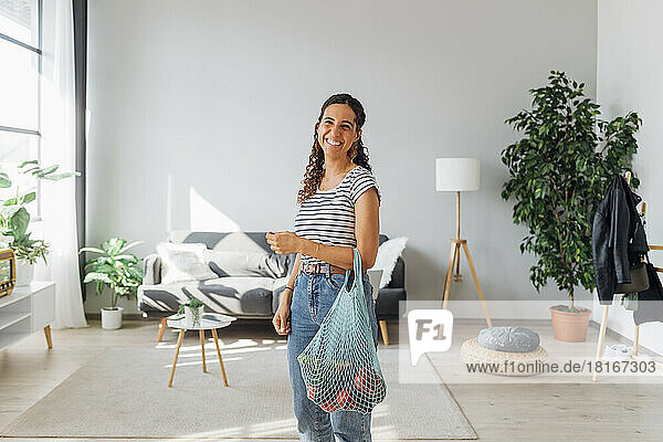 Happy woman with vegetables in mesh bag at home