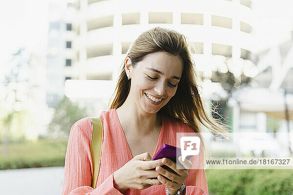 Happy woman using smart phone in front of building
