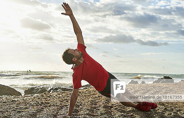 Mann macht Dehnübungen am Strand an einem sonnigen Tag