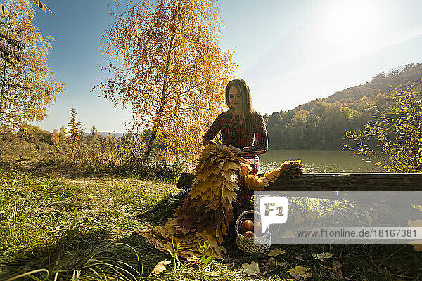 Frau mit gelben Blättern strickt Schal auf Baumstamm im Park