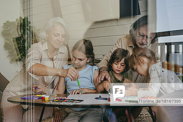 Grandparents with kids painting at home seen through glass of window