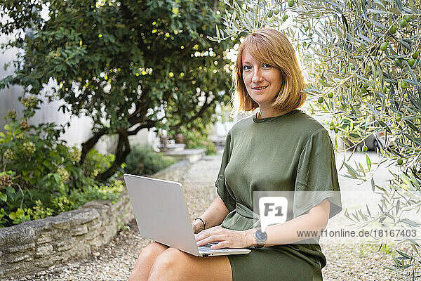 Smiling freelancer sitting with laptop in garden