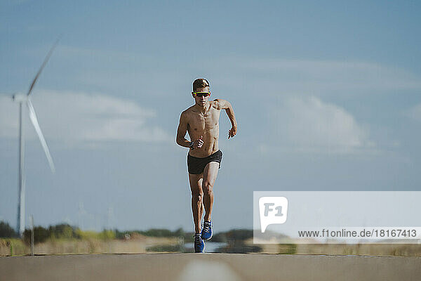 Shirtless fit athlete running on road in front of sky
