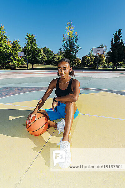 Young basketball player with ball sitting on court