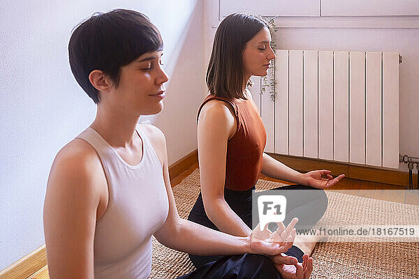 Smiling women with eyes closed meditating at home