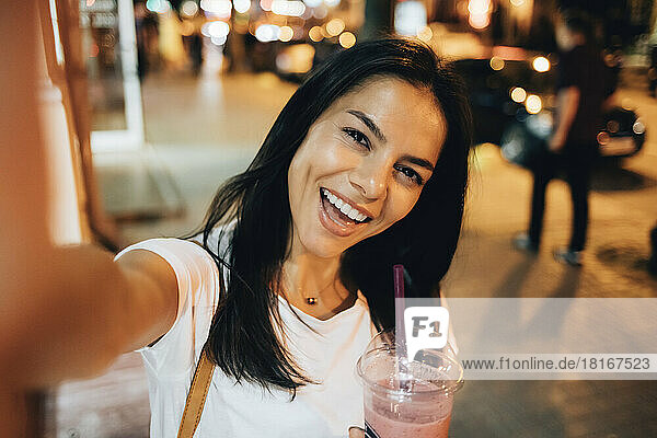 Fröhliche Frau mit Smoothie  die nachts ein Selfie macht