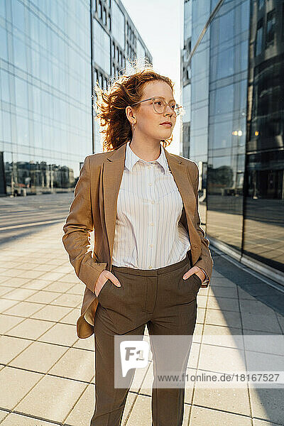 Confident businesswoman with hands in pockets standing on footpath