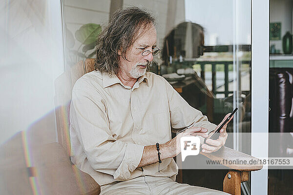 Senior man using tablet PC sitting on chair at home