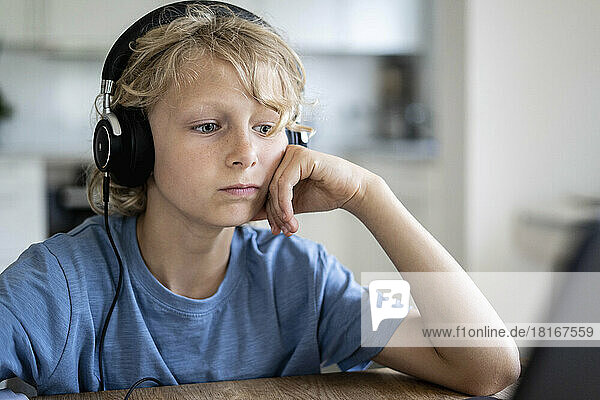 Junge mit kabelgebundenen Kopfhörern stützt sich am Tisch auf den Ellenbogen