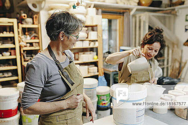 Töpfer und Kollege gießen Ton in Plastikbecher in der Keramikwerkstatt