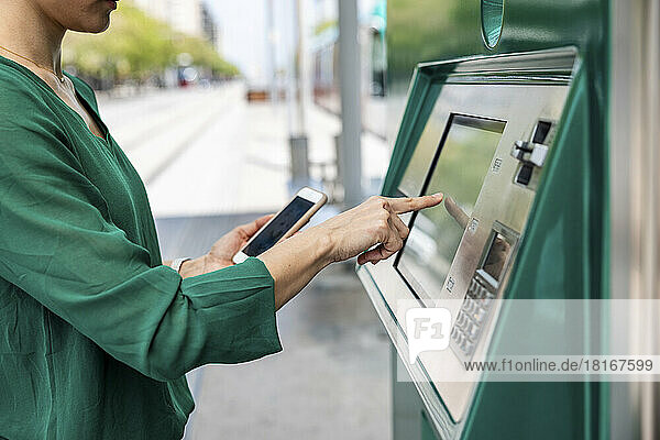 Frau mit Smartphone am Fahrkartenautomaten