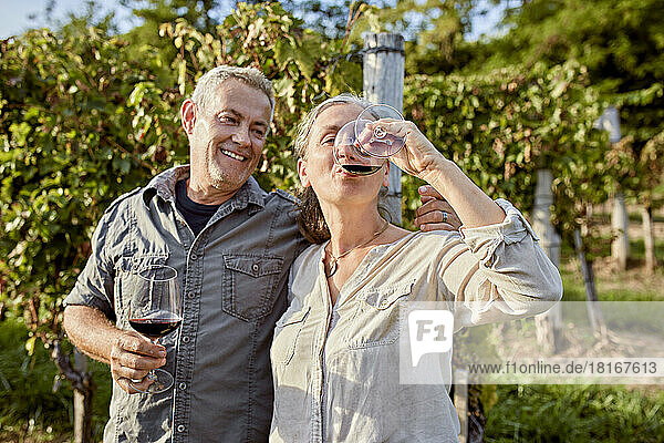 Smiling mature man holding wineglass looking at woman drinking wine in front of vineyard