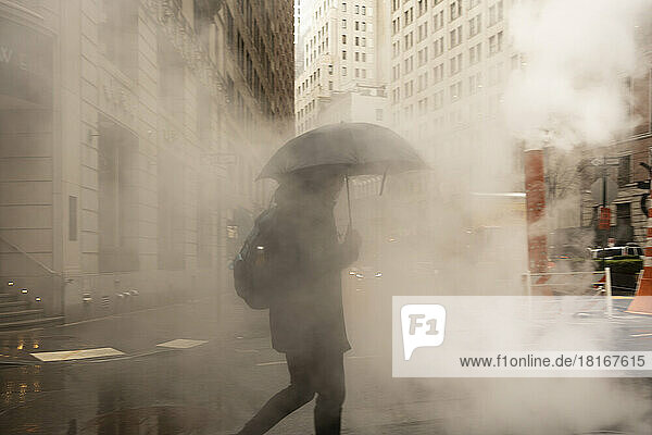 USA  New York  New York City  Pedestrian walking with umbrella across street covered in smoke