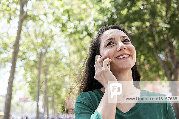 Happy woman talking on smart phone in front of tree