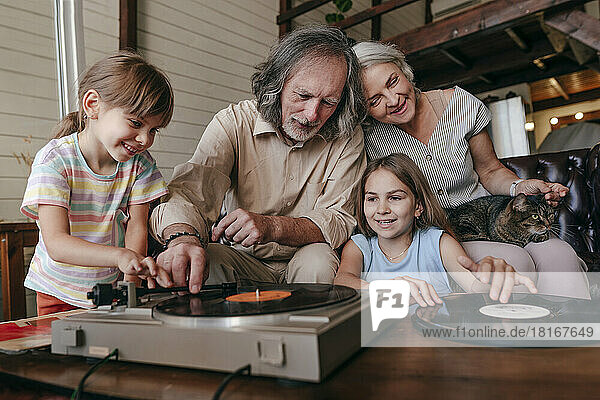 Grandfather with granddaughters playing music on vinyl record player at home