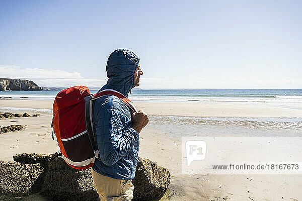Mann mit Rucksack steht an einem sonnigen Tag am Strand