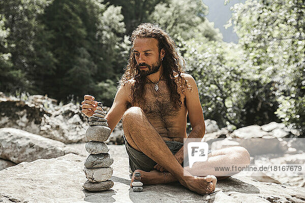 Shirtless young hipster stacking stones on rock