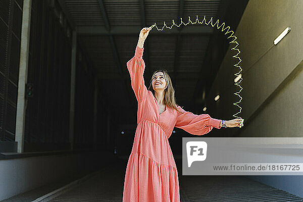 Playful woman playing with metal coil toy on footpath