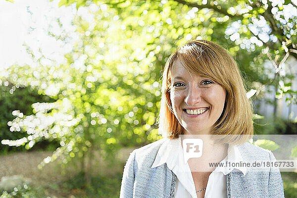 Smiling mature businesswoman in redhead standing in garden