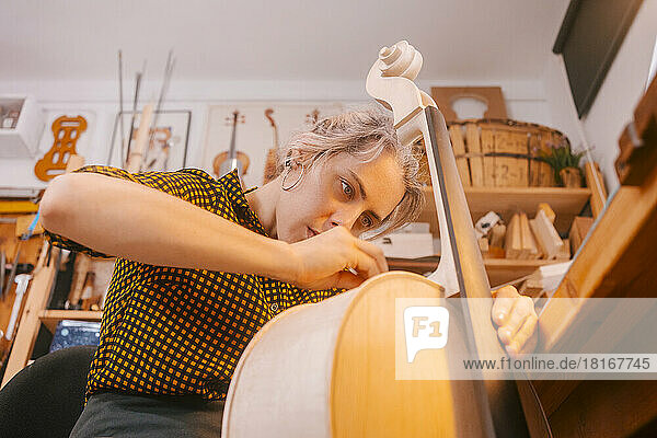 Luthier working on double bass in musical instrument workshop