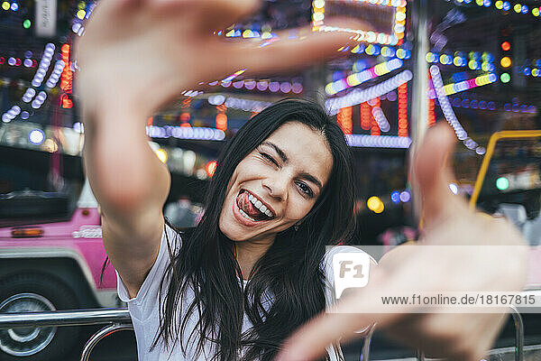 Cheerful woman winking and looking through finger frame at amusement park