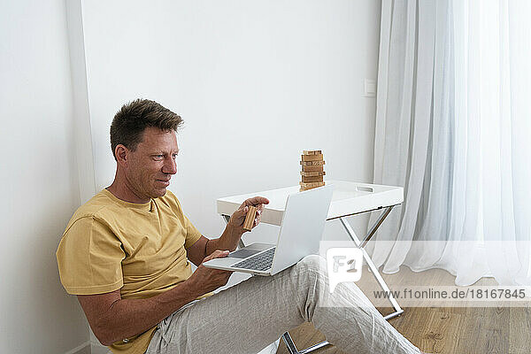 Smiling mature man showing toy block on video call through laptop at home