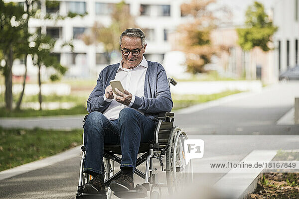 Smiling senior man using smart phone sitting on wheelchair